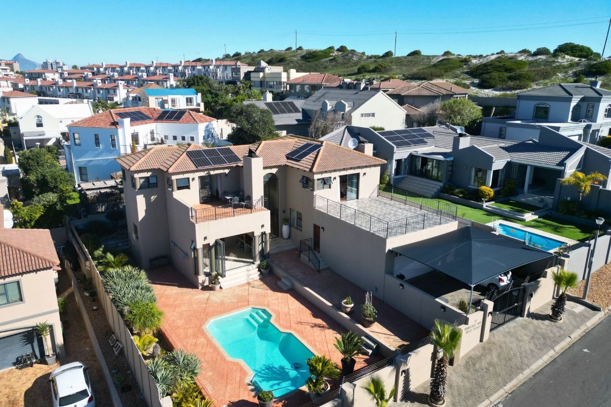 Aerial view of a multi-level residential property featuring a swimming pool, paved patio, upper-level balconies, solar panels, and a covered carport.