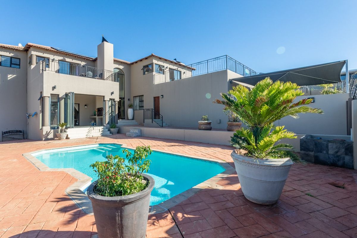 Rear exterior view featuring a swimming pool, paved patio area, and a multi-level house with balconies and a chimney.
