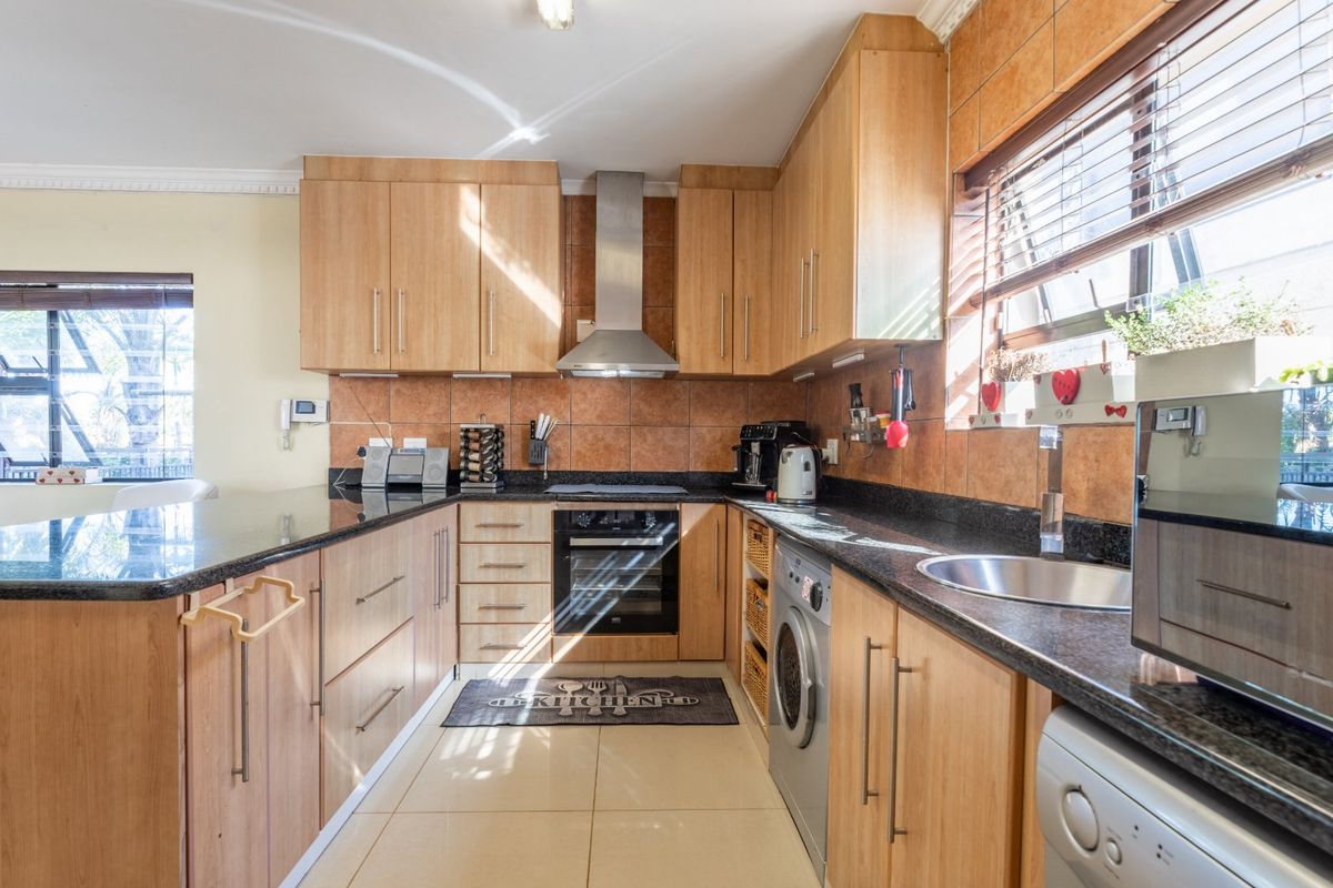 Functional kitchen featuring light wood cabinetry, granite countertops, tiled backsplash, built-in oven, extractor fan, and integrated laundry appliance space.