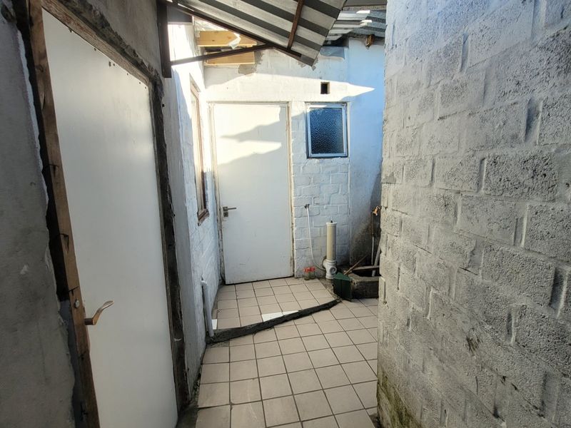 A functional outdoor utility or service area featuring tiled flooring, exposed brick walls, and direct access to the property's exterior.