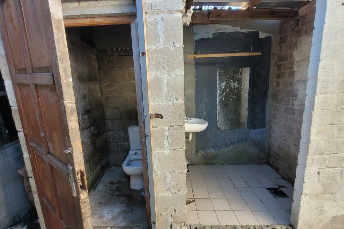 A basic, unfinished bathroom featuring exposed concrete block walls, a standard toilet, and a wall-mounted washbasin with tiled flooring.
