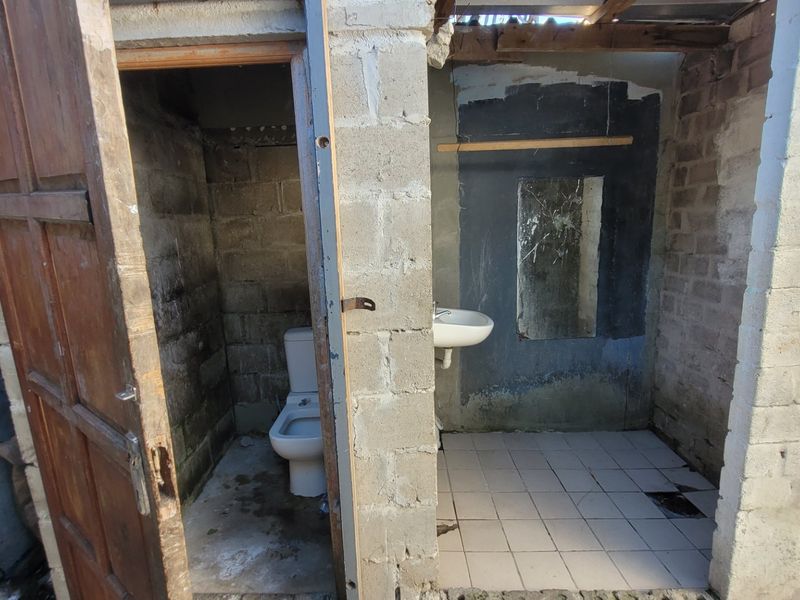 A basic, unfinished bathroom featuring exposed concrete block walls, a standard toilet, and a wall-mounted washbasin with tiled flooring.