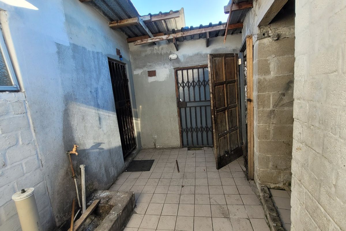 An exterior rear utility area featuring tiled flooring, a concrete basin, and security gates, requiring maintenance and structural repairs to the roof and walls.