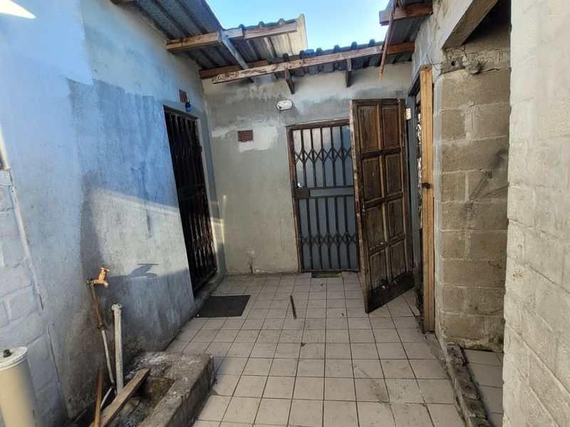 An exterior rear utility area featuring tiled flooring, a concrete basin, and security gates, requiring maintenance and structural repairs to the roof and walls.