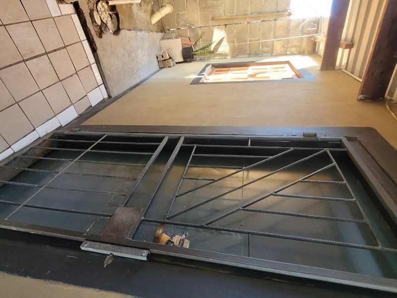 An unfinished outdoor patio area featuring a security gate, tiled flooring, and exposed concrete block walls, requiring significant cosmetic completion.