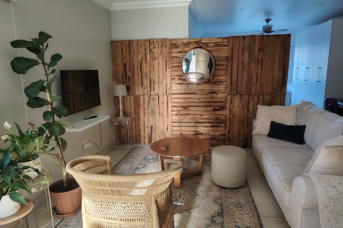 A comfortable living room featuring tiled flooring, crown molding, and a ceiling fan, with a rustic wooden partition wall creating a distinct living space.