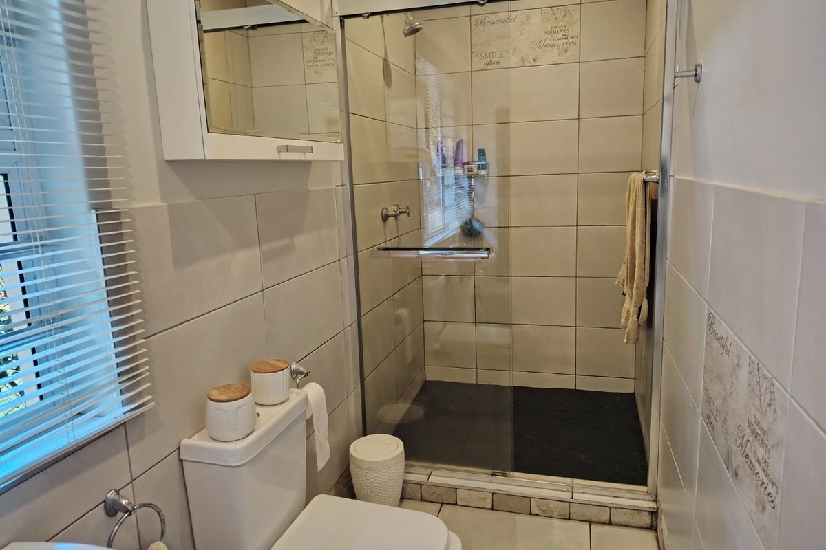 A functional bathroom featuring a glass-enclosed shower, neutral wall tiling, and a wall-mounted medicine cabinet.