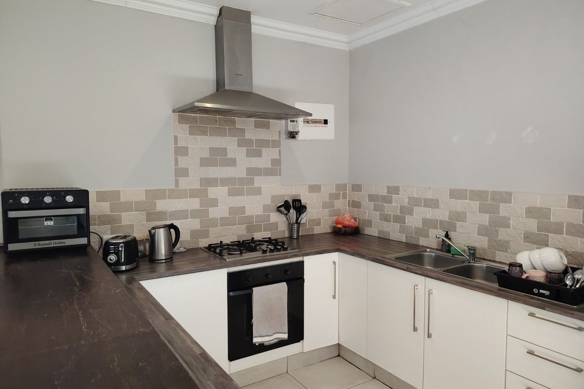 A functional kitchen featuring white cabinetry, dark laminate countertops, a gas hob with extractor fan, and a tiled backsplash.