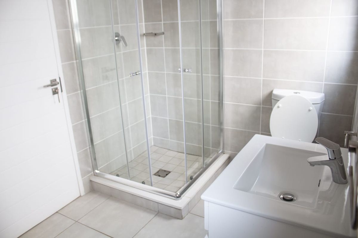 A clean, modern bathroom featuring a glass shower enclosure, a white vanity basin with mixer tap, and neutral wall and floor tiling.