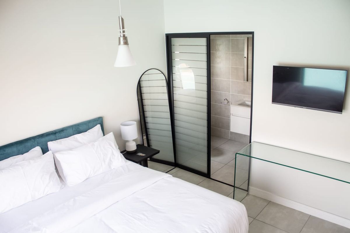 Modern bedroom featuring tiled flooring, a wall-mounted television, and a sliding glass door providing direct access to an en-suite bathroom.