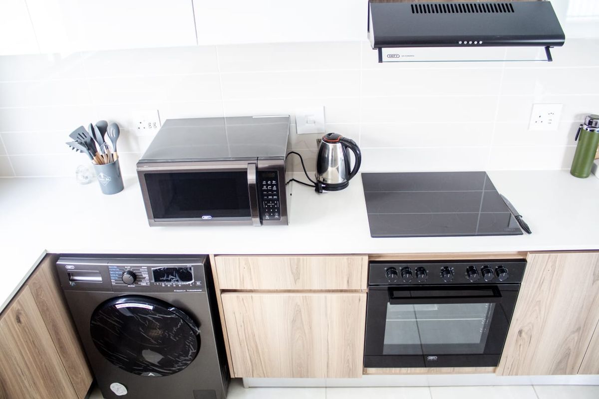 Modern kitchen featuring light wood cabinetry, white tiled backsplash, built-in oven, electric hob, extractor fan, and an integrated washing machine.