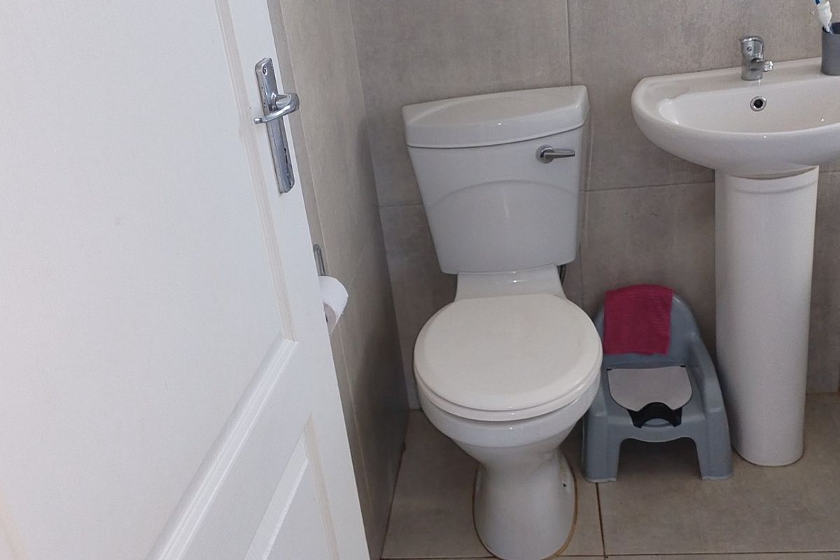 A functional bathroom featuring a pedestal basin, toilet, and bathtub with neutral wall and floor tiling.