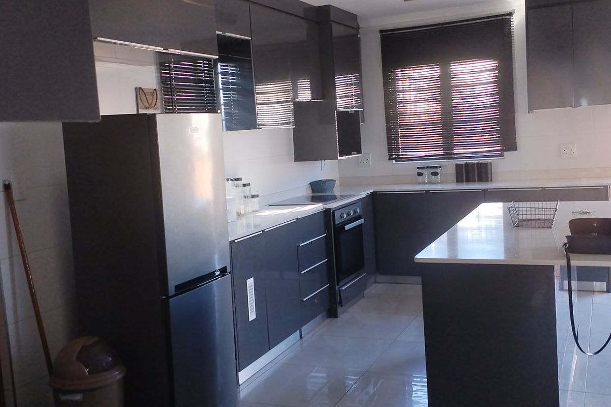 Modern kitchen featuring dark grey cabinetry, stone countertops, a central island, and built-in appliances with tiled flooring and natural light.