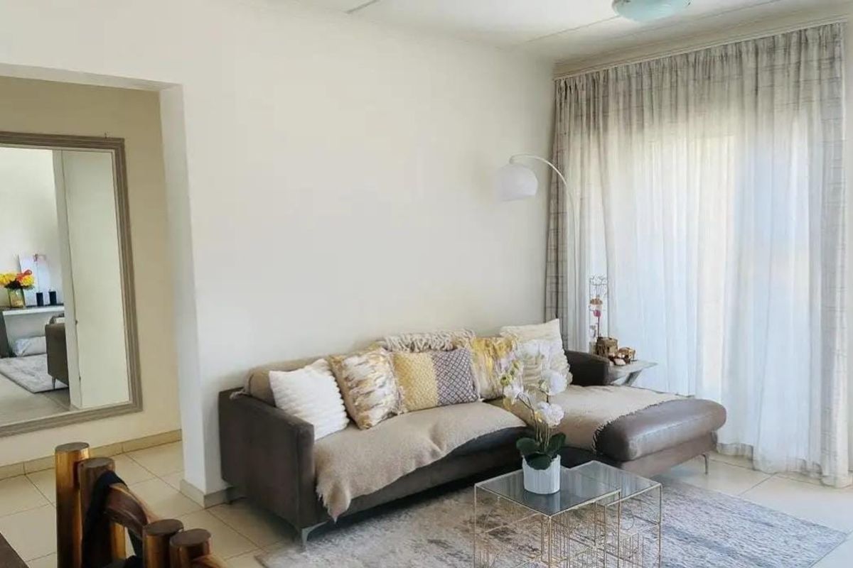 A bright living room featuring tiled flooring and a large sliding glass door with curtains, providing access to the outdoor area.