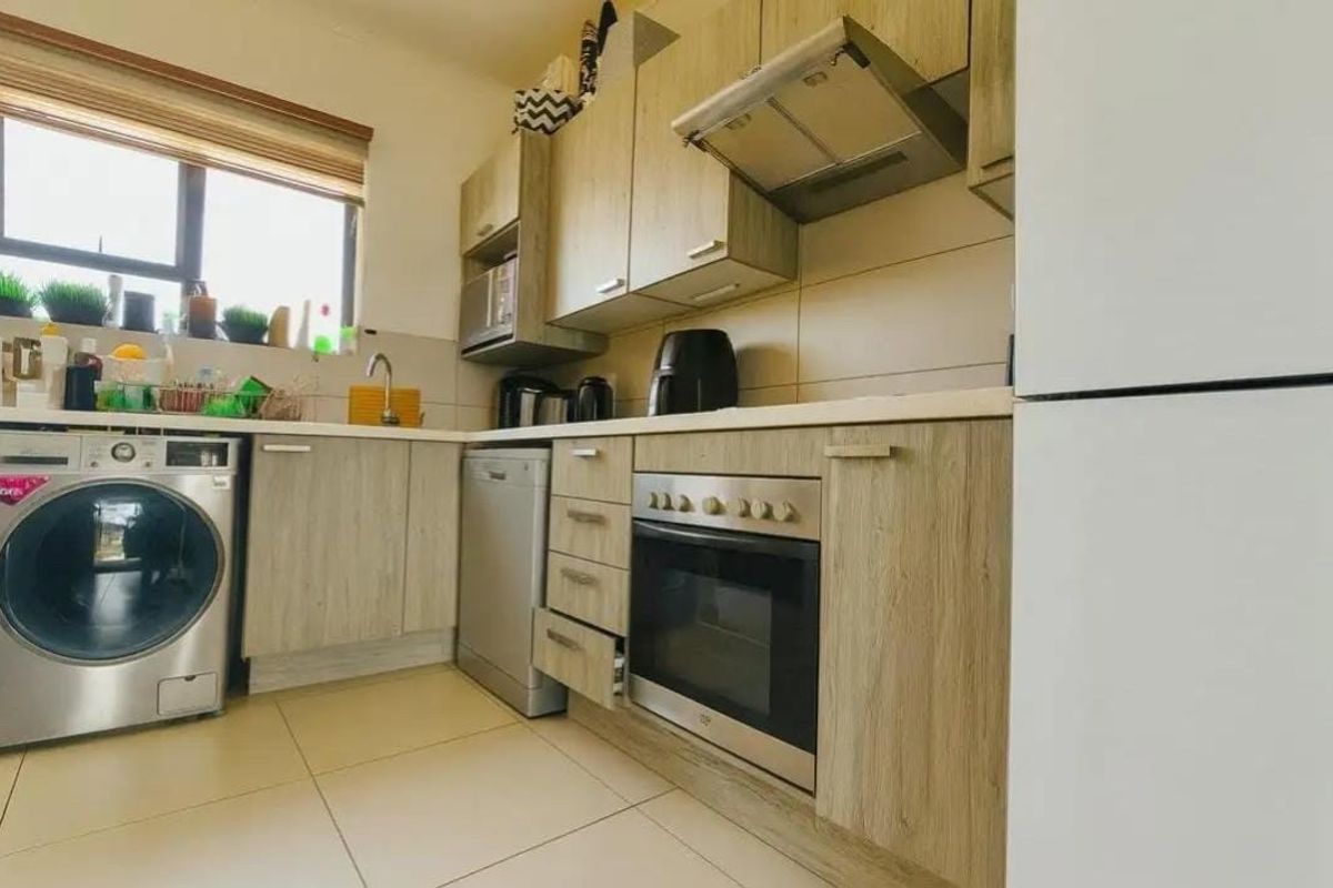 A functional kitchen featuring light wood-tone cabinetry, tiled flooring, built-in oven with extractor fan, and integrated space for laundry appliances.