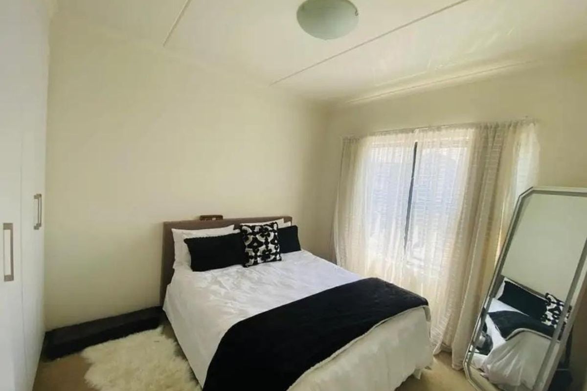 A functional bedroom featuring a built-in wardrobe and natural light through a window with sheer curtains.