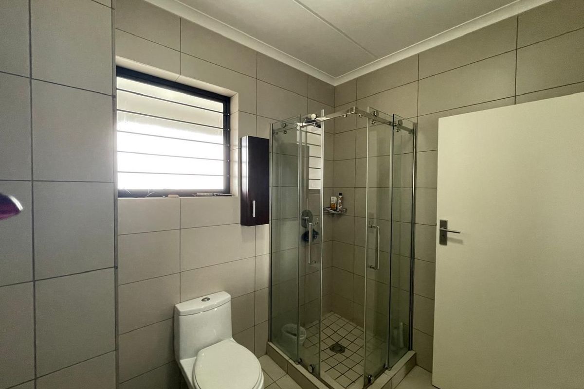 A functional bathroom featuring a glass shower enclosure, a modern toilet, and neutral wall and floor tiling.