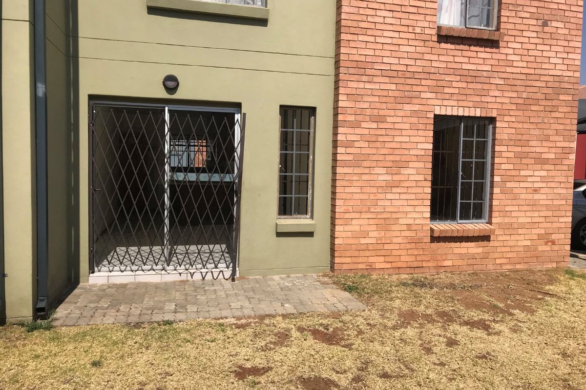 Rear exterior view of the apartment featuring a paved patio area, sliding glass door with security gate, and a combination of brick and painted masonry.
