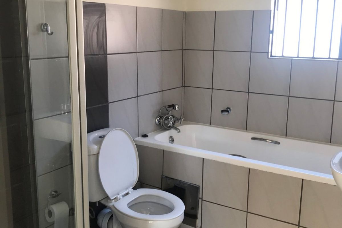 A functional bathroom featuring a bathtub, separate shower enclosure, toilet, and an exposed electric water heater unit.