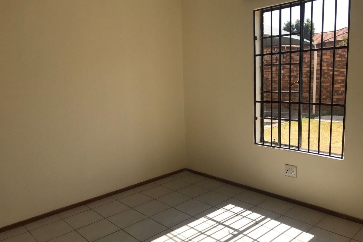 An empty bedroom featuring tiled flooring, a window with security bars, and neutral wall finishes, offering a blank canvas for personalization.