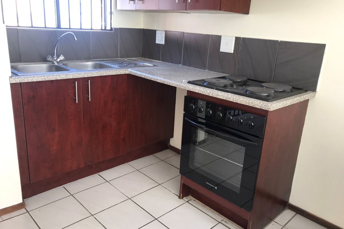 A functional kitchen featuring dark wood-finish cabinetry, stone-look countertops, a built-in electric oven with hob, and tiled flooring.
