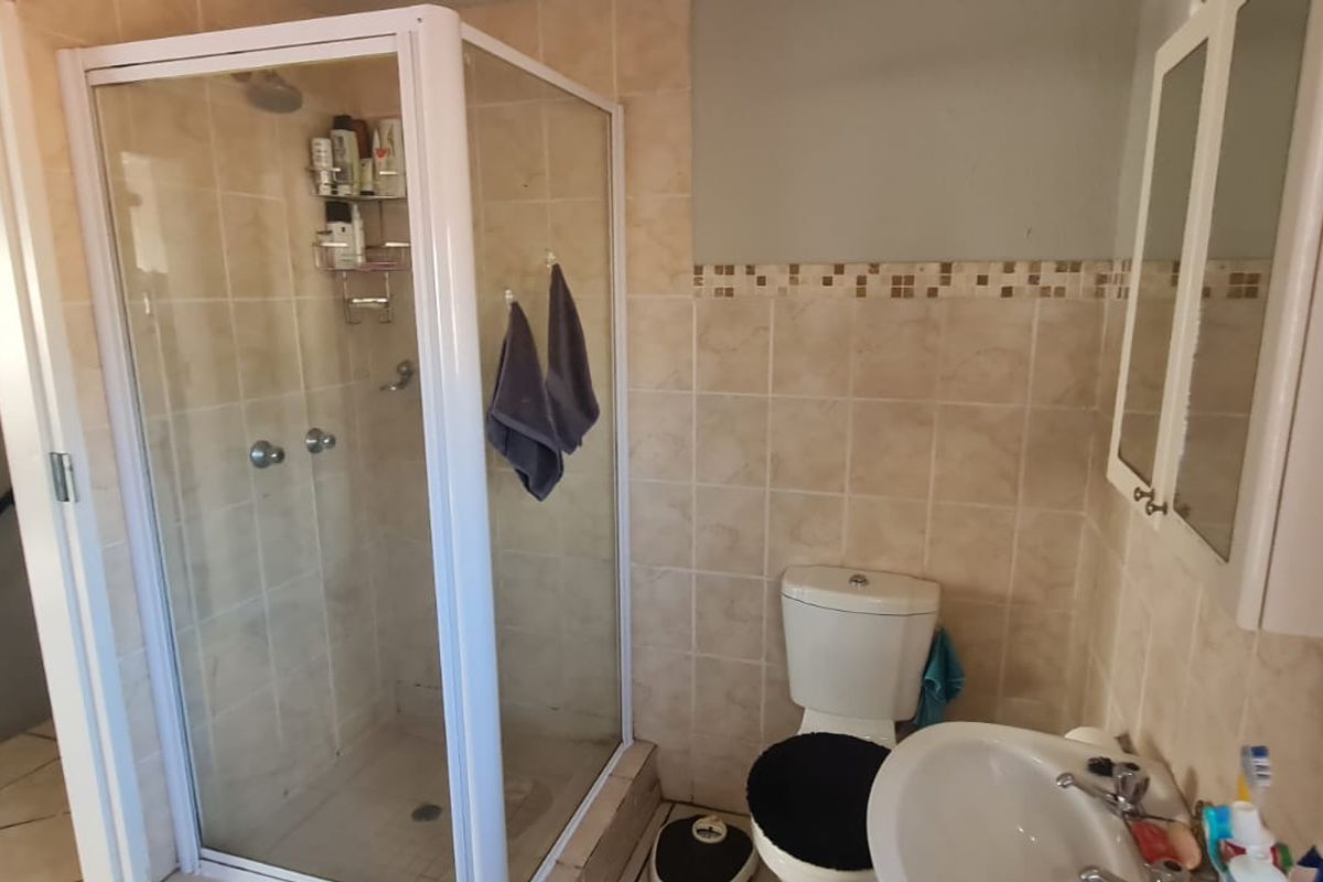 A functional bathroom featuring a corner shower enclosure, pedestal basin, toilet, and tiled wall finishes with a built-in medicine cabinet.