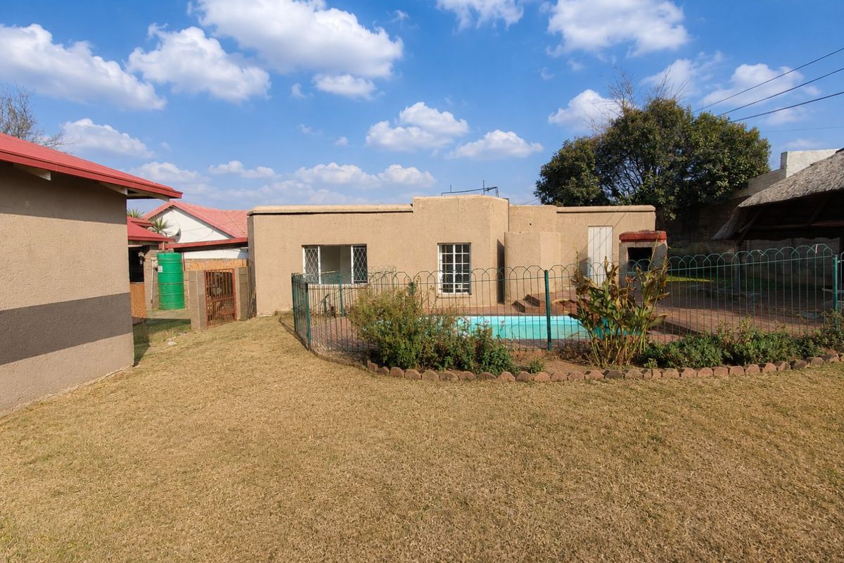 Rear garden area featuring a swimming pool, built-in braai, metal fencing, and a thatched lapa structure.