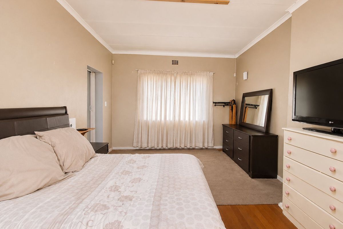 A spacious bedroom featuring a mix of timber and carpet flooring, neutral wall tones, and a large window with fitted curtain tracks.