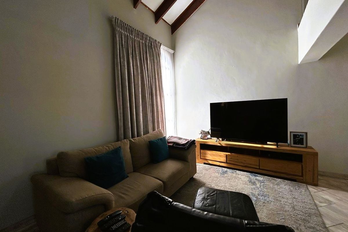 Spacious living room featuring high vaulted ceilings with exposed timber beams and neutral tiled flooring, creating an airy and open atmosphere.