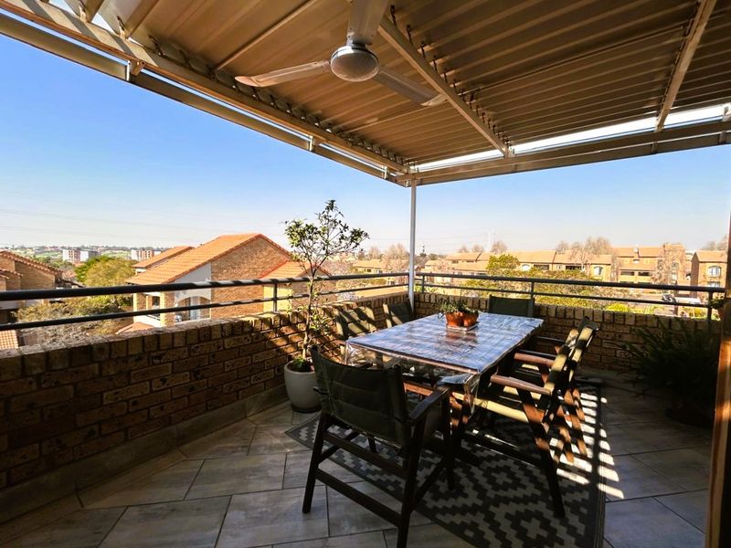 A spacious covered balcony featuring tiled flooring, a ceiling fan, and a brick balustrade, offering elevated views of the surrounding neighborhood.