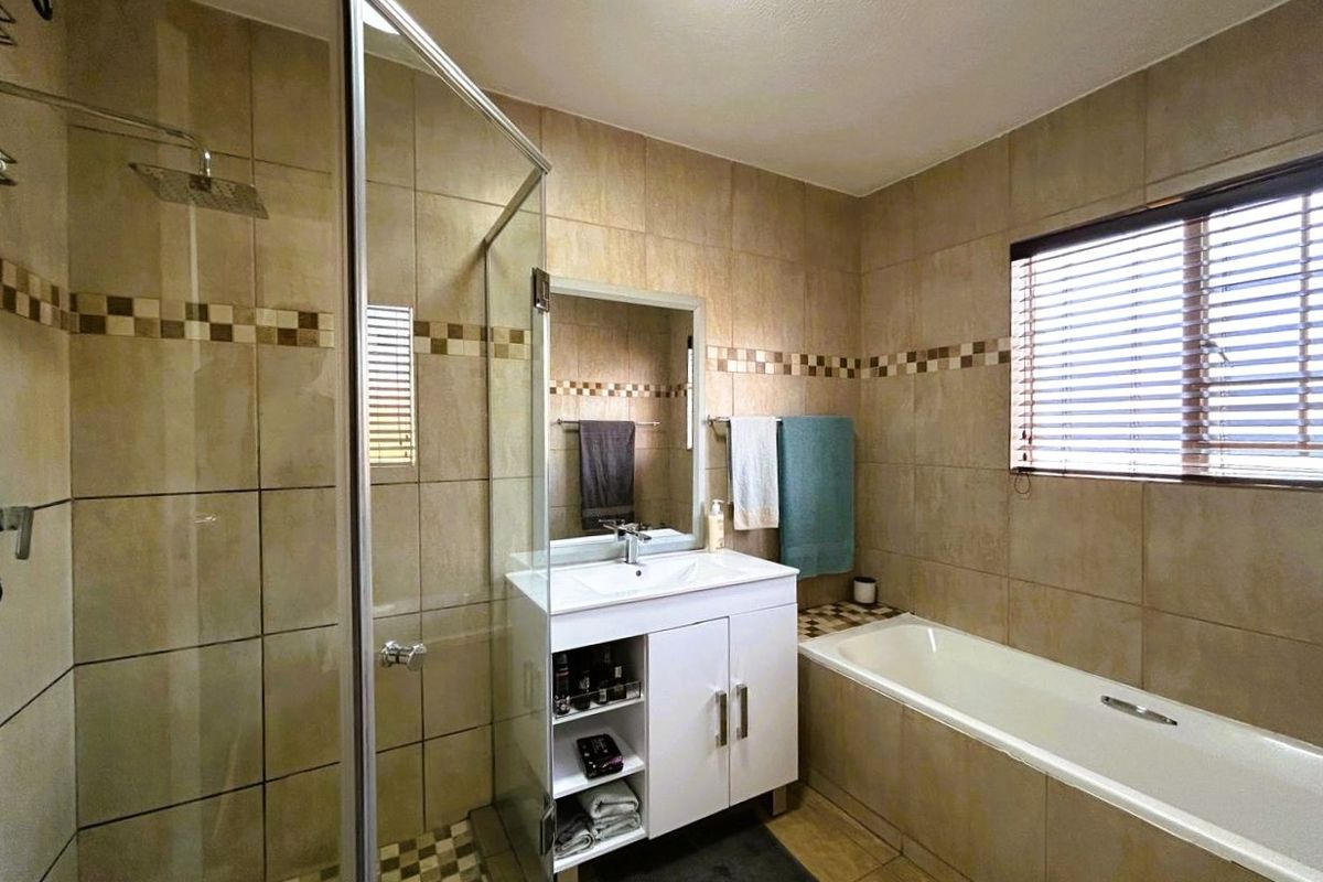 A well-maintained bathroom featuring a glass-enclosed shower, a built-in bathtub, and a modern vanity cabinet with tiled finishes throughout.