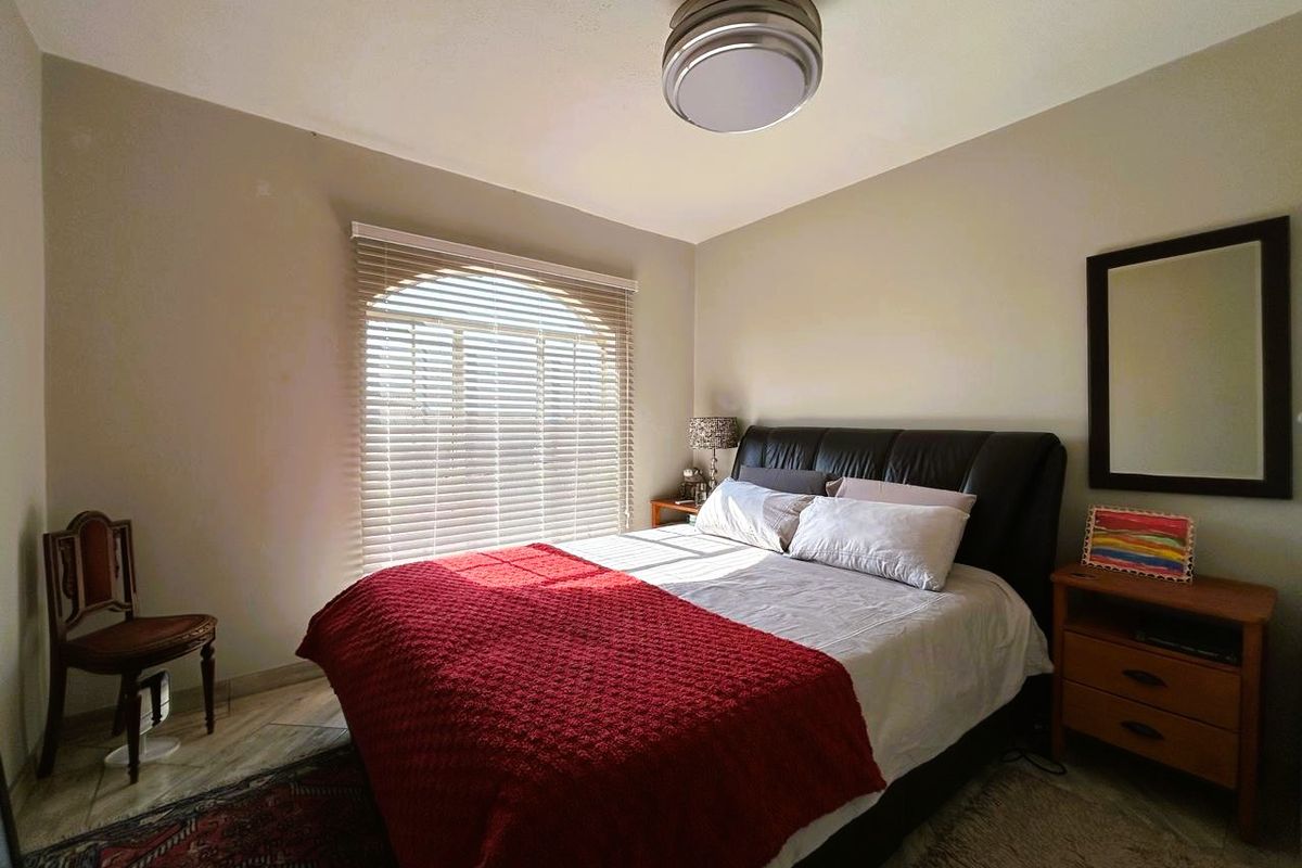 A well-lit bedroom featuring tiled flooring, an arched window with venetian blinds, and a central flush mount ceiling light fixture.