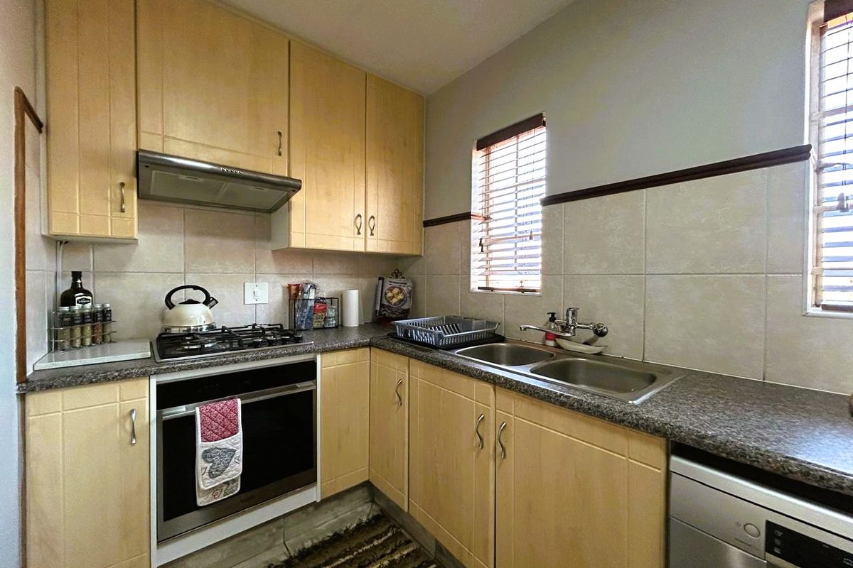 A functional kitchen featuring light wood cabinetry, granite-look laminate countertops, a gas hob, built-in oven, and a stainless steel double sink with tiled backsplash.