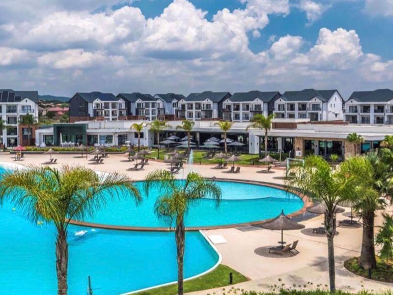 A large, well-maintained swimming pool area surrounded by landscaped gardens and modern multi-story apartment buildings.