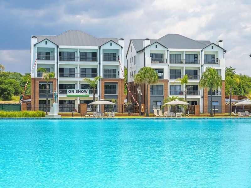A view of modern multi-story apartment buildings overlooking a large, clear swimming pool with landscaped surroundings.