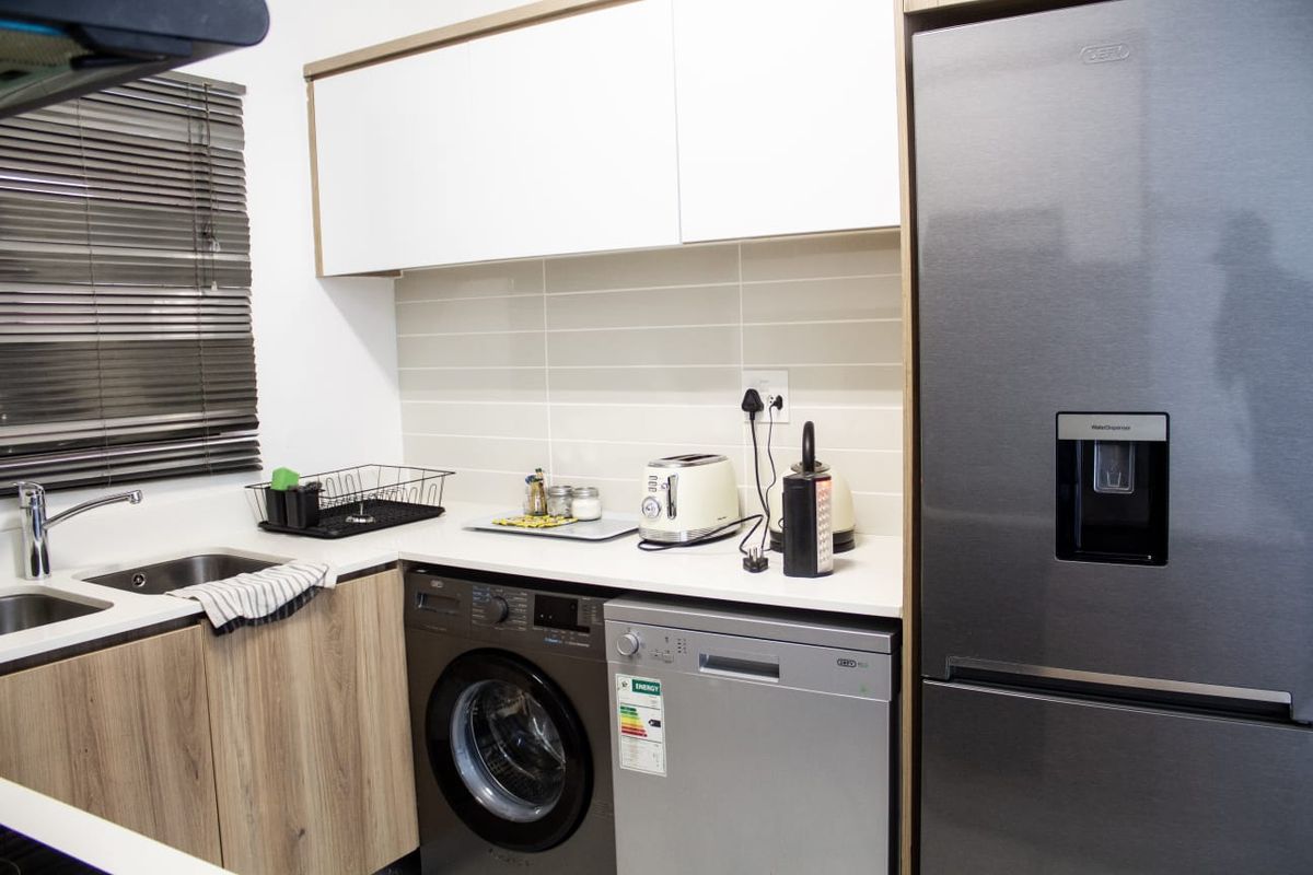 Modern kitchen featuring sleek white and wood-grain cabinetry, subway tile backsplash, stainless steel sink, and integrated appliances including a washing machine and dishwasher.