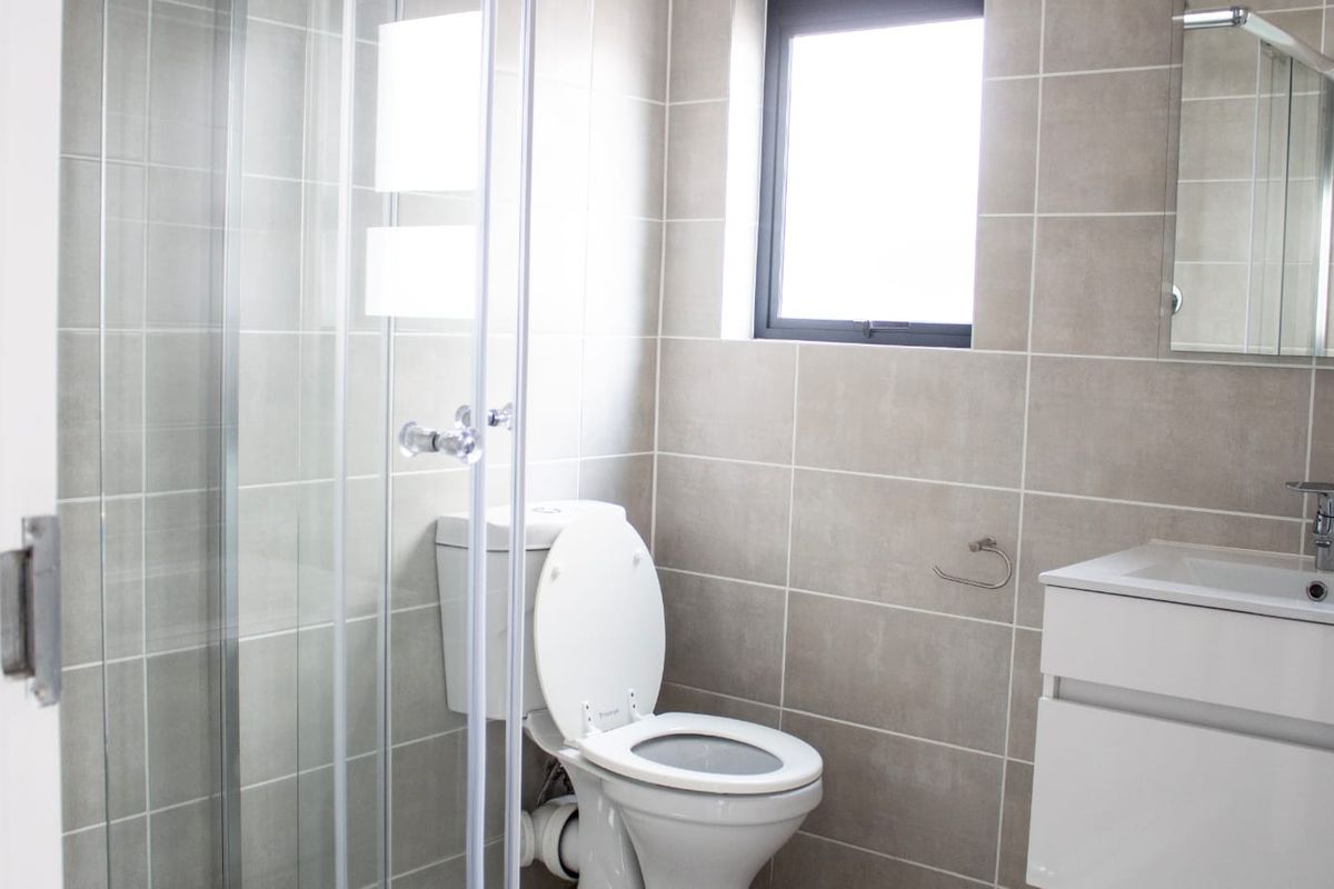 A modern, clean bathroom featuring a glass shower enclosure, a white vanity unit with basin, and neutral wall tiling.
