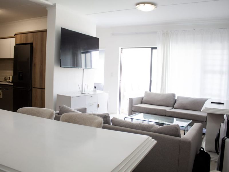 Modern open-plan living area featuring a contemporary kitchen with wood-finish cabinetry, flowing into a bright lounge space with direct access to a balcony.