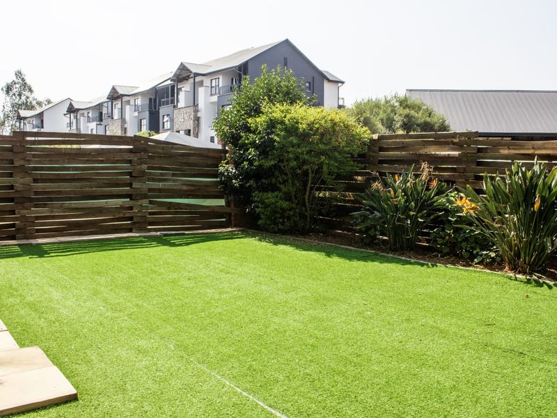 A well-maintained private garden featuring artificial turf, timber slat fencing, and established landscaping, providing a neat outdoor space.