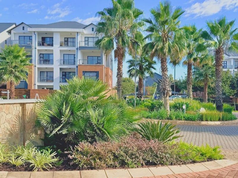 A well-maintained apartment complex exterior featuring landscaped gardens, paved driveways, and modern multi-story residential buildings with private balconies.