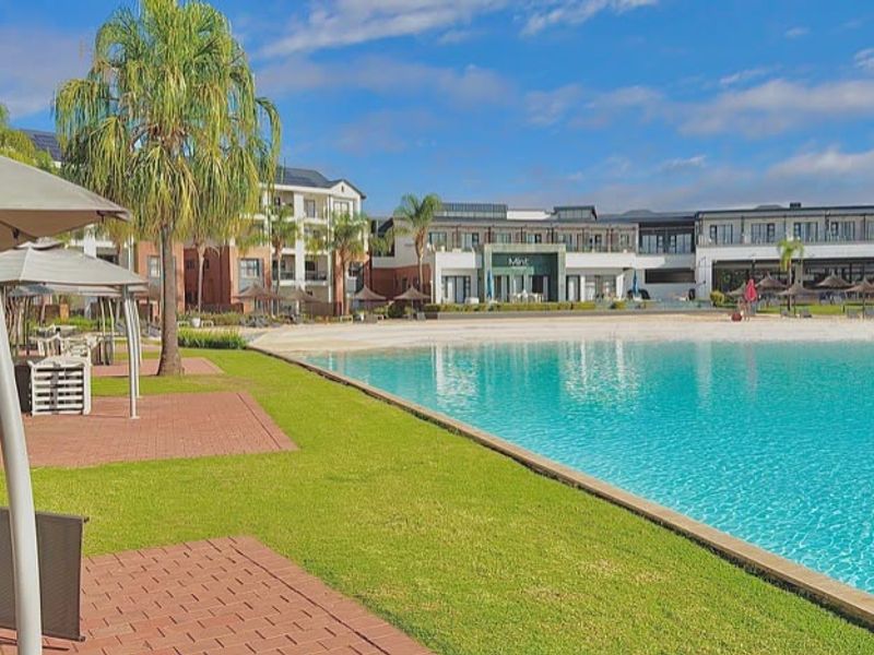 A well-maintained communal swimming pool area featuring a large pool, paved walkways, and landscaped green spaces within the apartment complex.