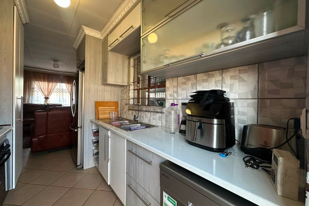 A functional kitchen featuring modern cabinetry, stone countertops, tiled backsplash, and ceramic flooring, with an open flow into the adjacent living area.