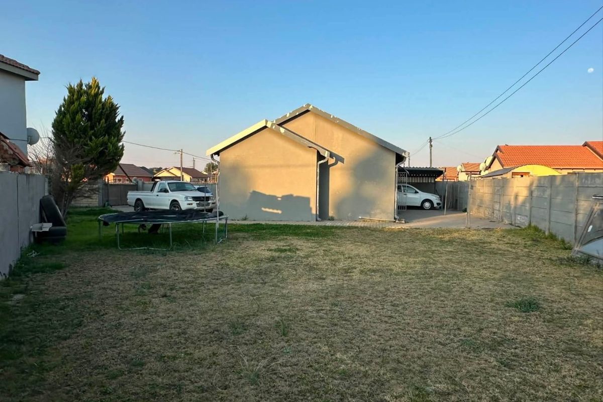 Rear view of the property featuring a private backyard with a lawn, paved driveway, and perimeter boundary walling.