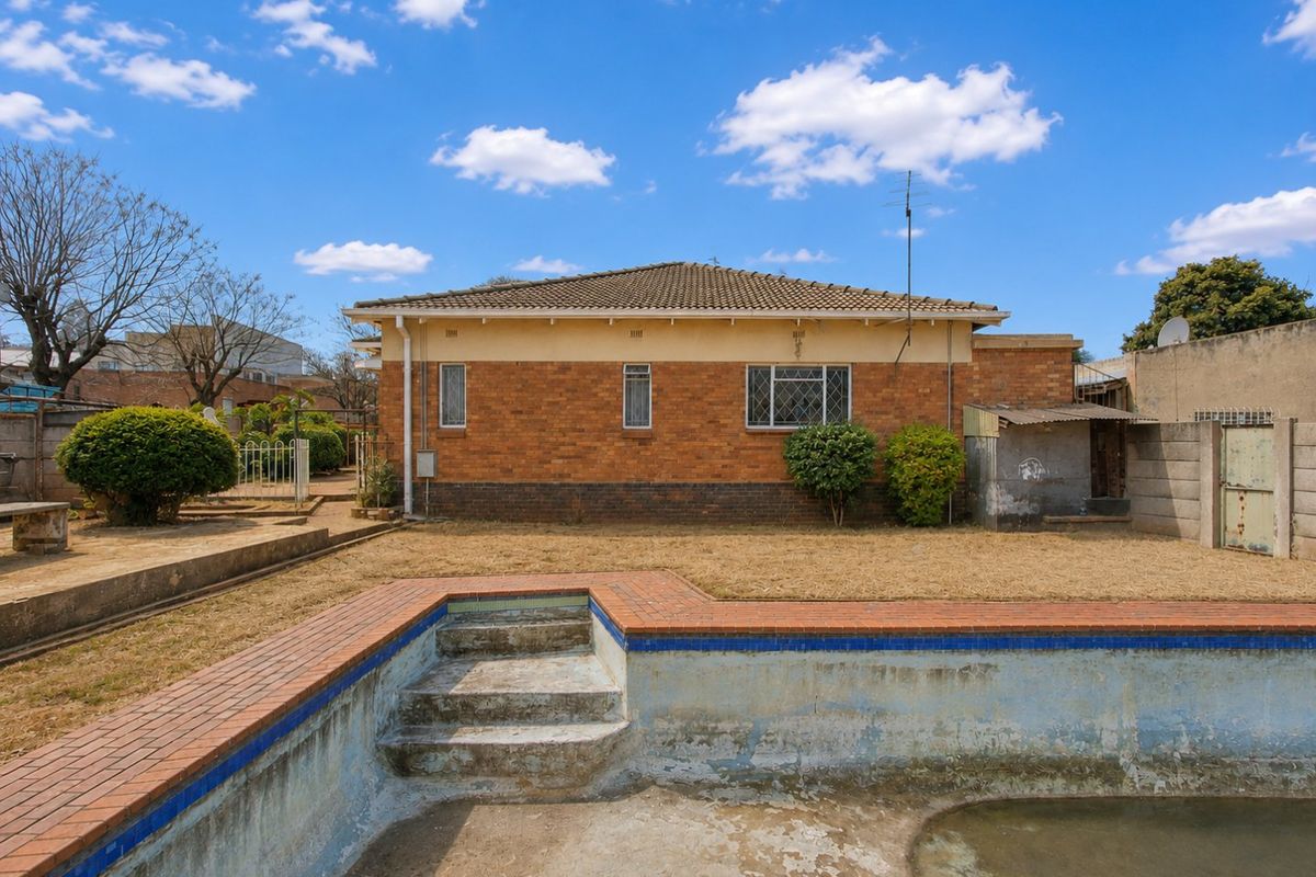 Rear view of a brick house featuring a swimming pool with brick coping and a surrounding garden area.