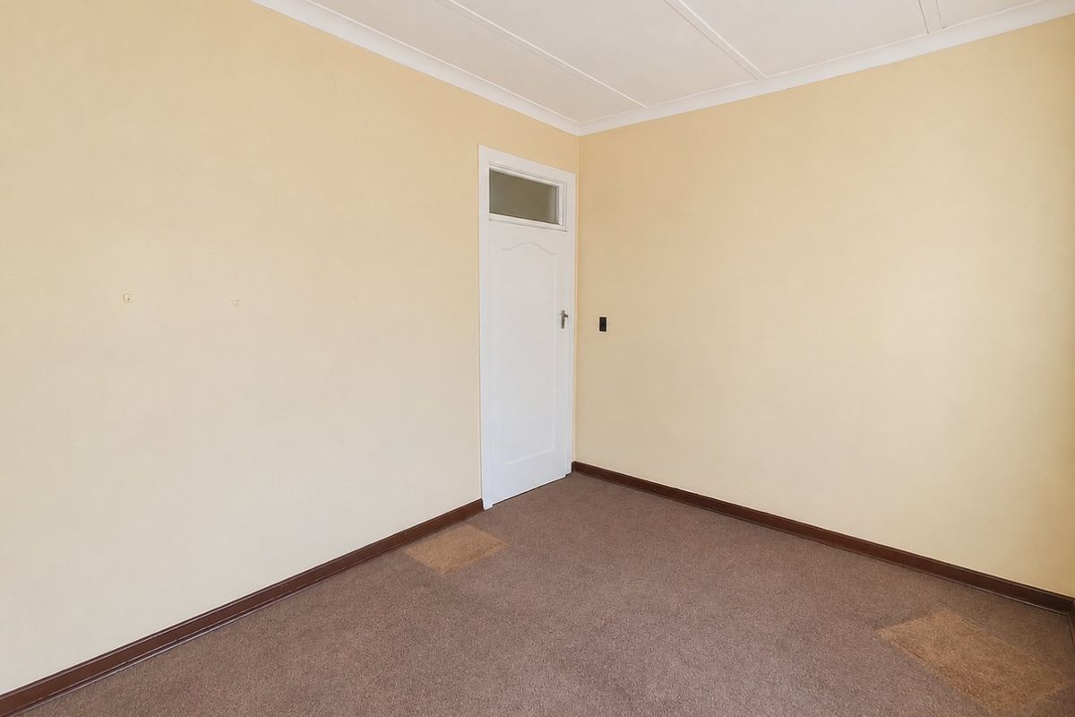 An empty bedroom featuring neutral walls, brown carpeting, and a classic internal door with a transom window.