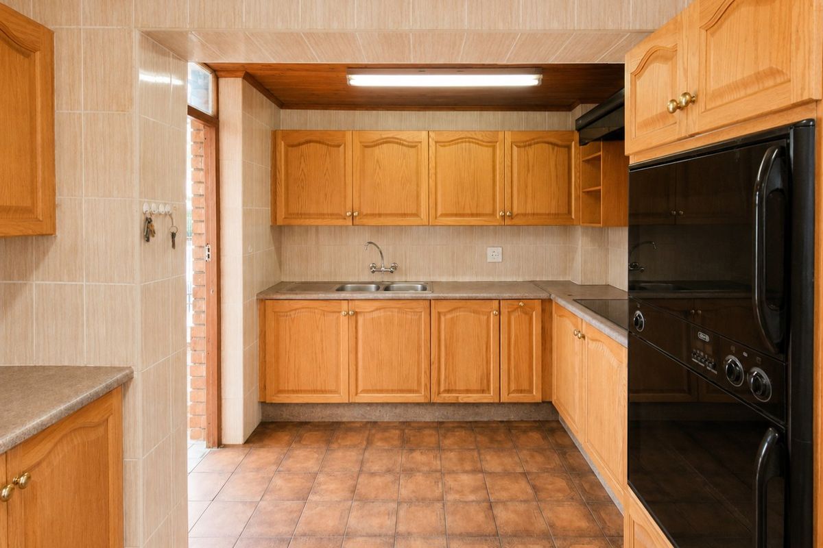 A functional kitchen featuring wooden cabinetry, laminate countertops, a double bowl sink, and a built-in oven with tiled finishes throughout.