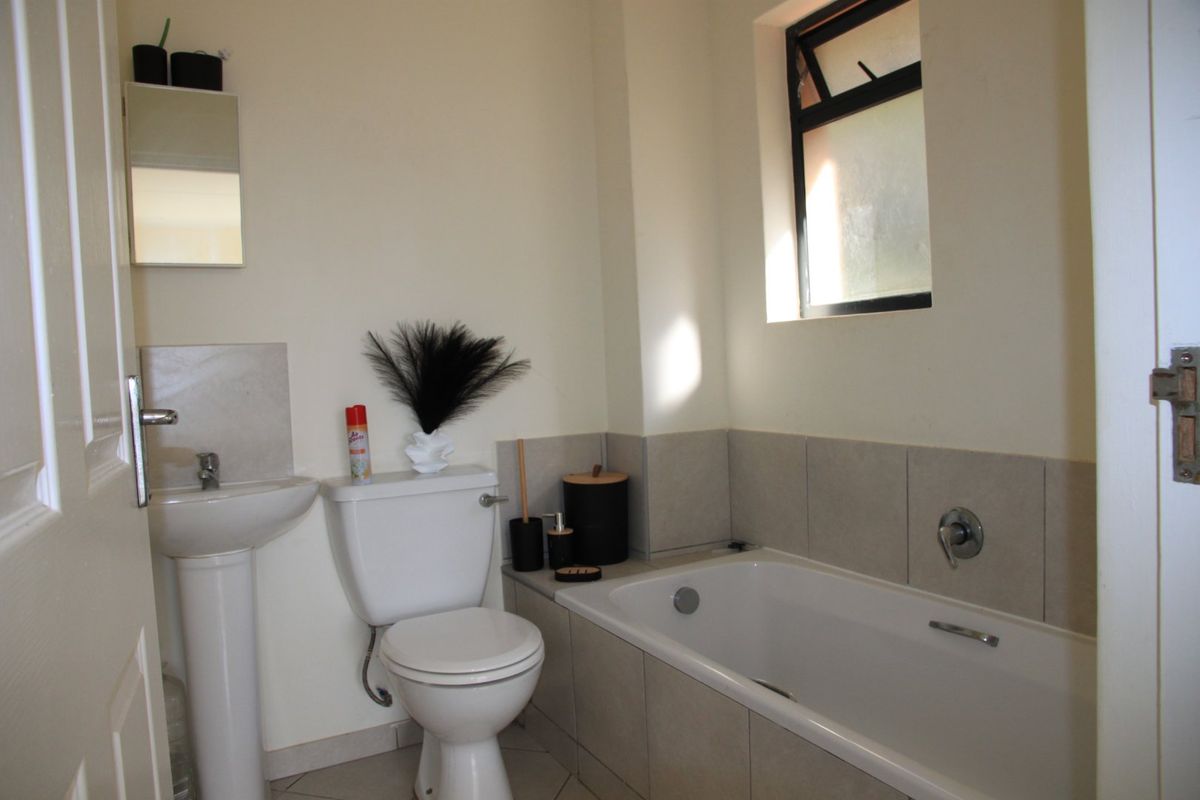 A functional bathroom featuring a pedestal basin, toilet, and a built-in bathtub with tiled splashbacks and a window for natural light.