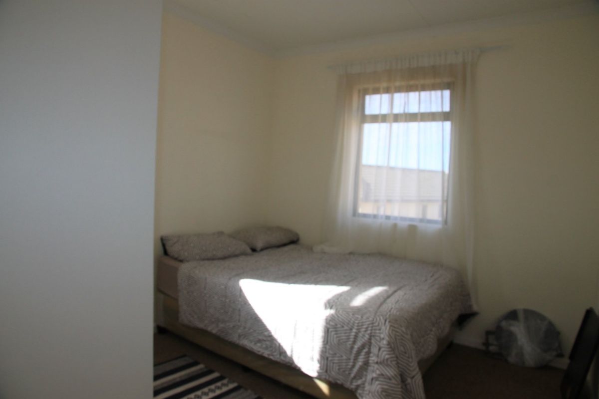 A simple bedroom featuring a window with natural light, neutral wall finishes, and carpeted flooring.