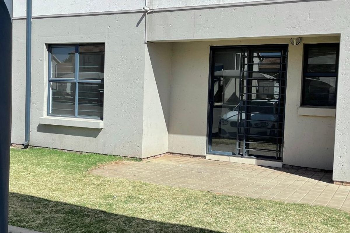 Ground floor apartment exterior featuring a paved patio, small lawn area, and an upper-level balcony with metal balustrades.
