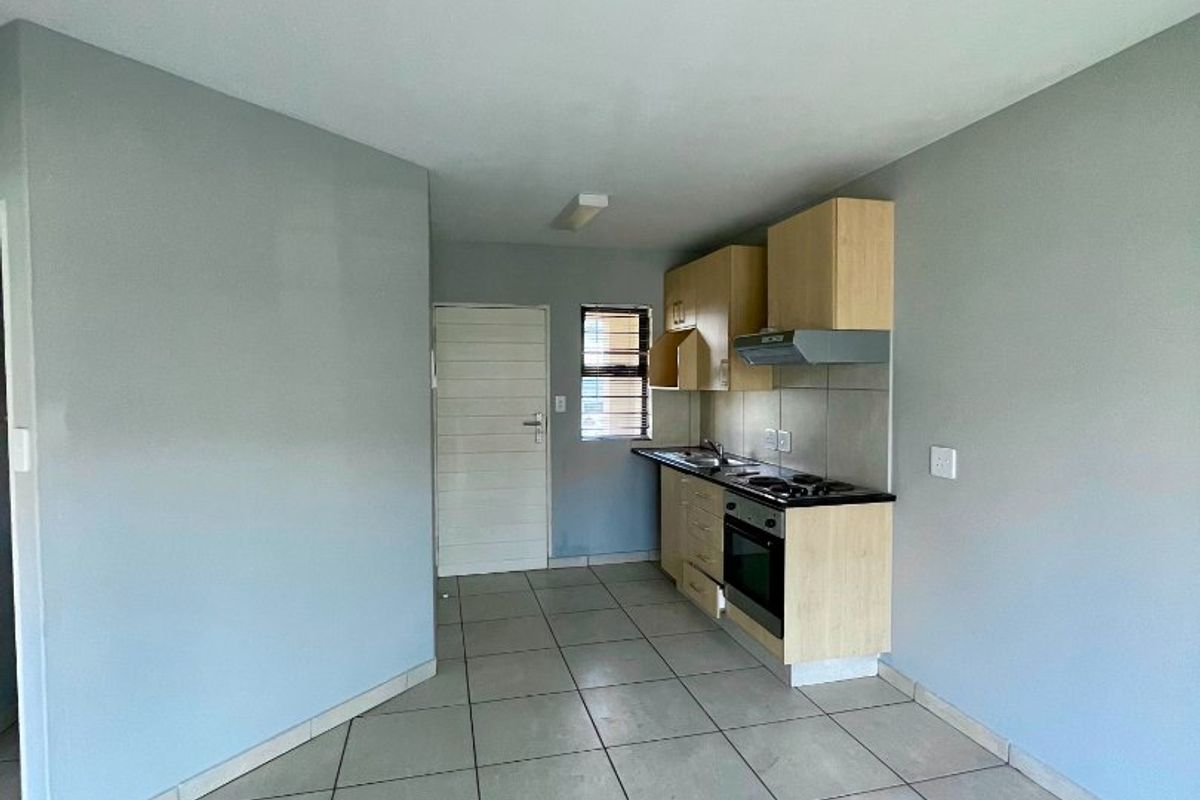 A compact, empty kitchen featuring light wood cabinetry, built-in oven, hob, extractor fan, and neutral tiled flooring.